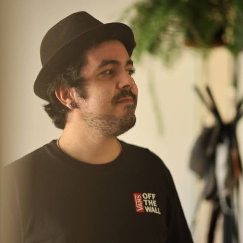 Rodrigo Santos, de chapéu e camiseta pretos, olhando para o lado, com plantas ao fundo