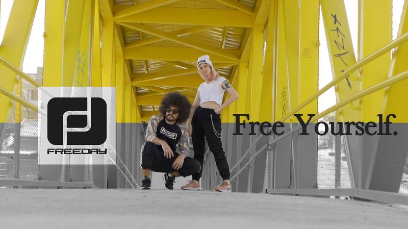 Quadro do filme Free Yourself, com um homem agachado e uma mulher em pé em uma passarela amarela, o logotipo da Freeday e o texto Free Yourself.