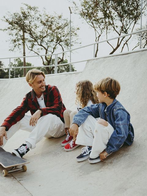 O pai e as crianças sentados na borda de uma rampa de skate, conversando e sorrindo, com tênis Vans nos pés.